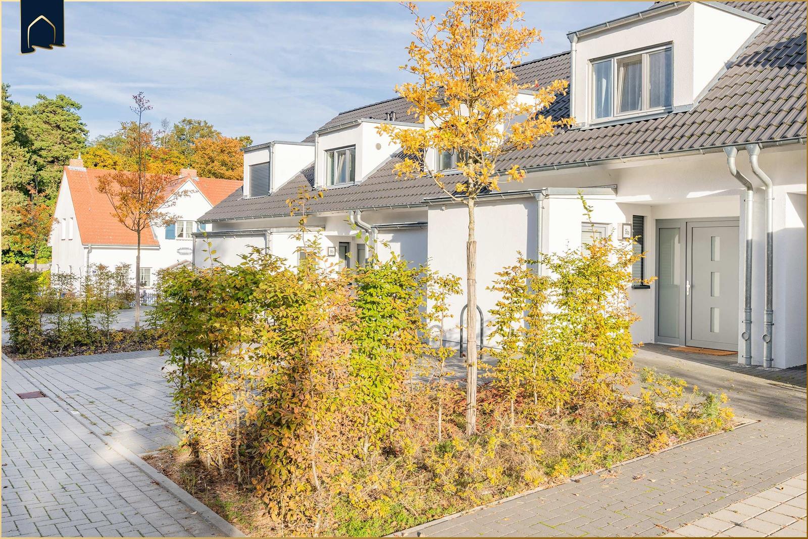 Moderne weiße Wohnhäuser mit grauem Dach und Bäumen im Herbst.