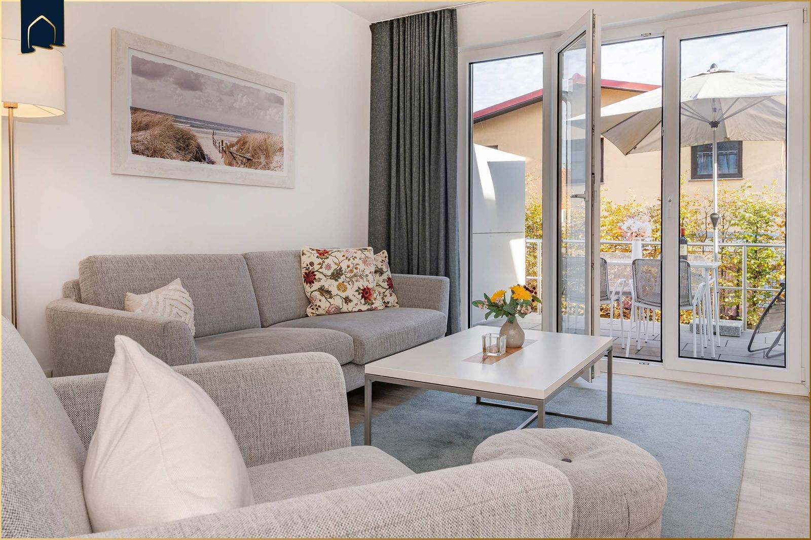 Wohnzimmer mit Sofa, Couchtisch und Blick auf Balkon mit Sonnenschirm.