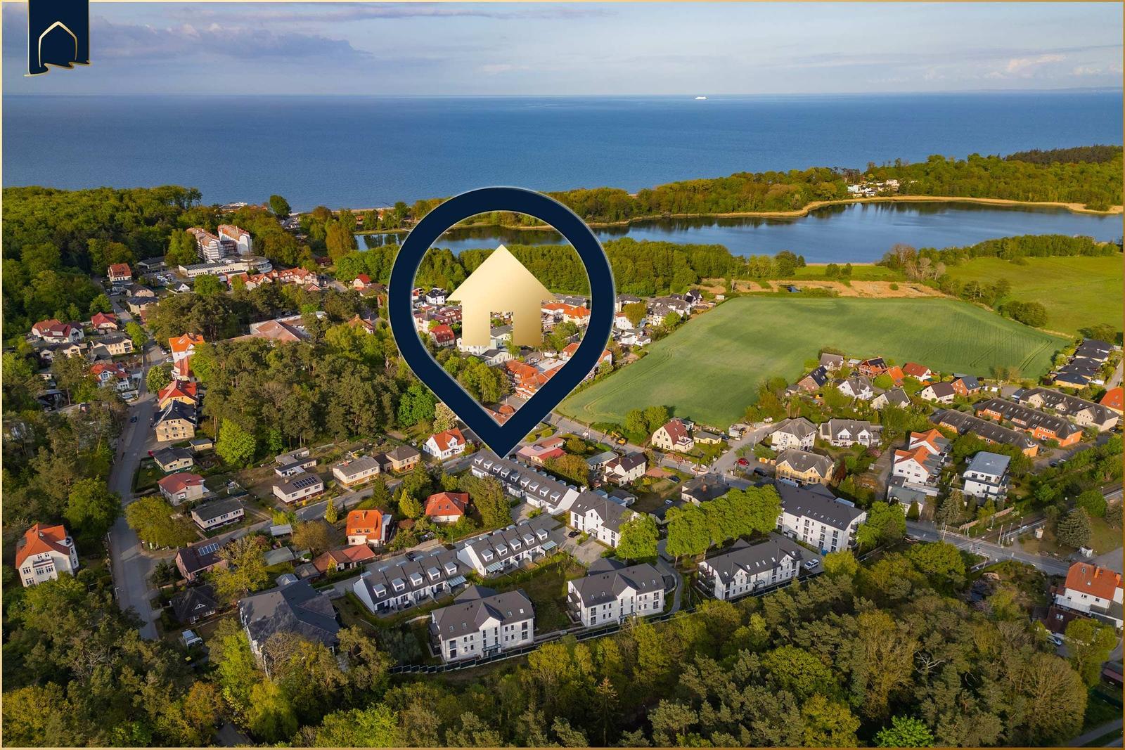 Luftbild einer Wohngegend mit Wald, Feldern und Blick aufs Meer.