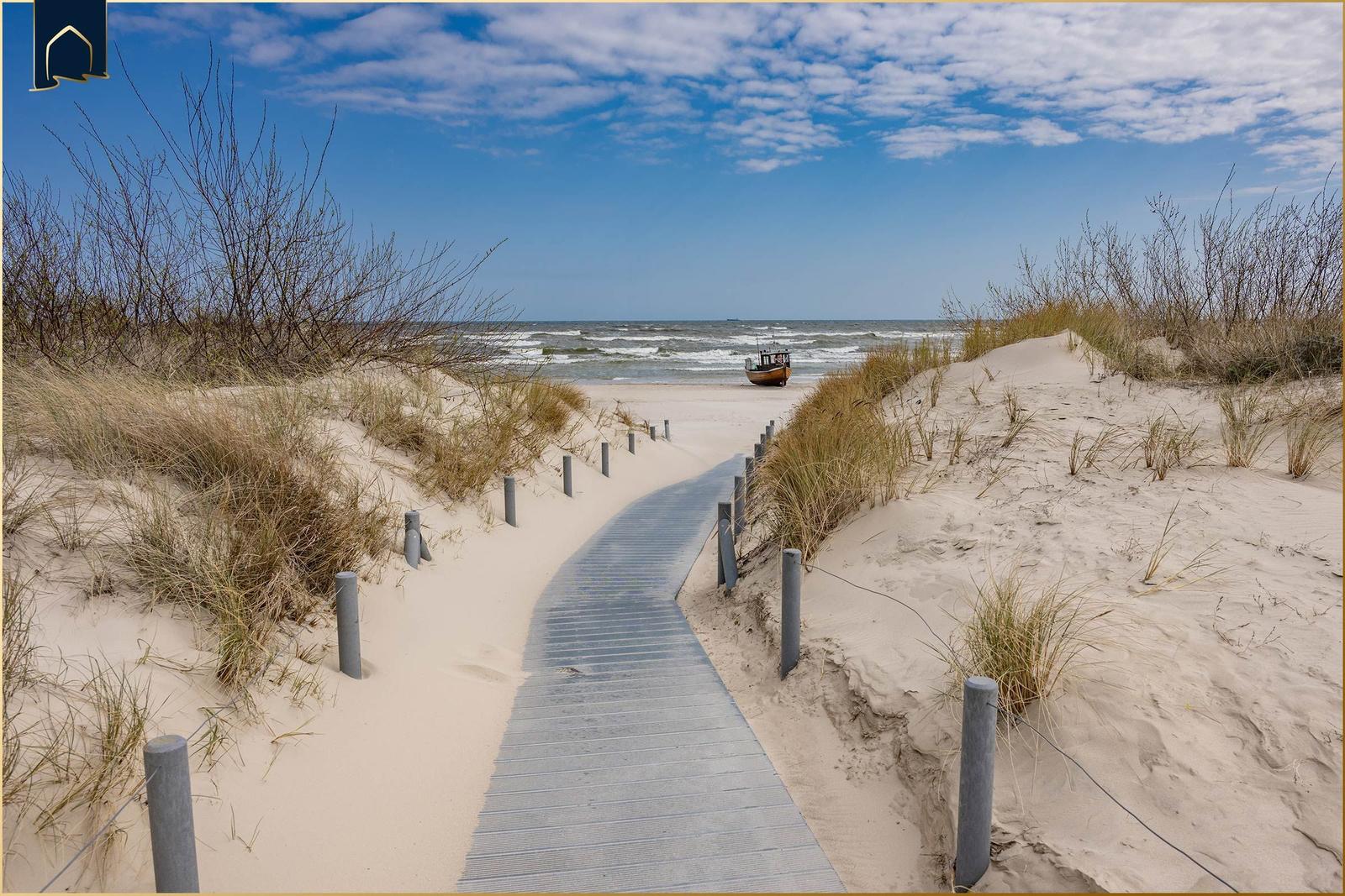 Holzweg durch Sanddünen zur See mit Fischerboot.