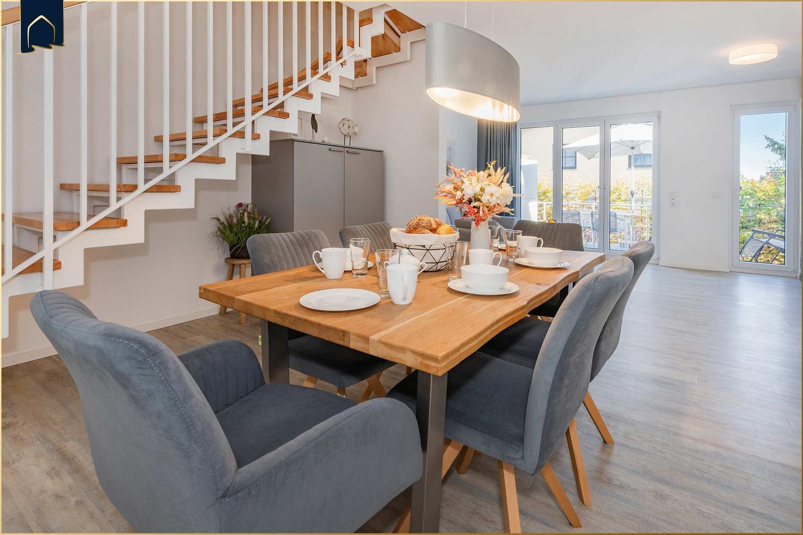 Essbereich mit Holztisch, grauen Stühlen und Blick auf Balkon.
