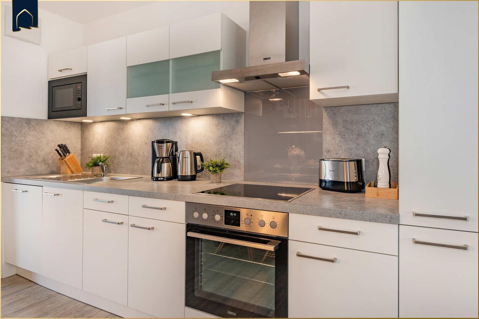 Küche mit weißen Schränken, Edelstahlgeräten und grauer Arbeitsplatte.