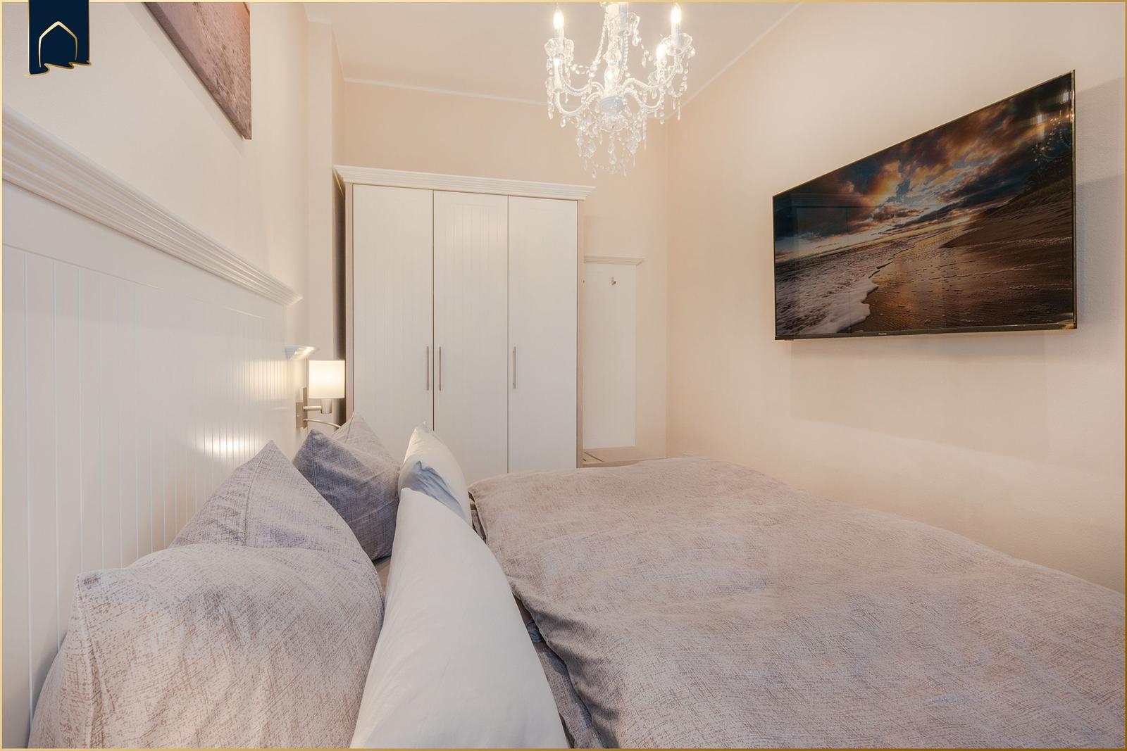 Schlafzimmer mit Bett, Kleiderschrank und Wandbild. Deckenleuchte und Wandlampe.