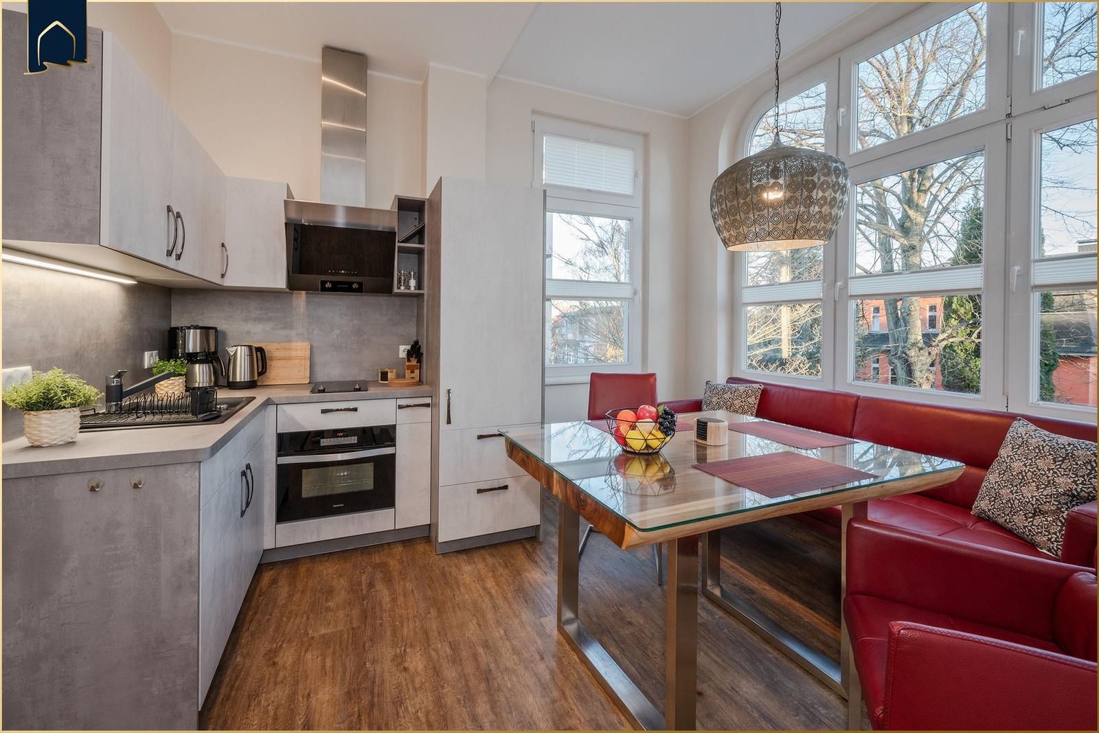 Küche mit Essbereich, rote Ledersitze und Glas-Tisch. Große Fenster mit Blick nach draußen.