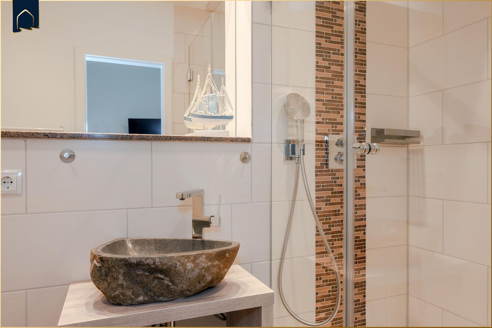 Bad mit Steinwaschbecken, Dusche und Spiegel. Wandverkleidung aus Steinfliesen.
