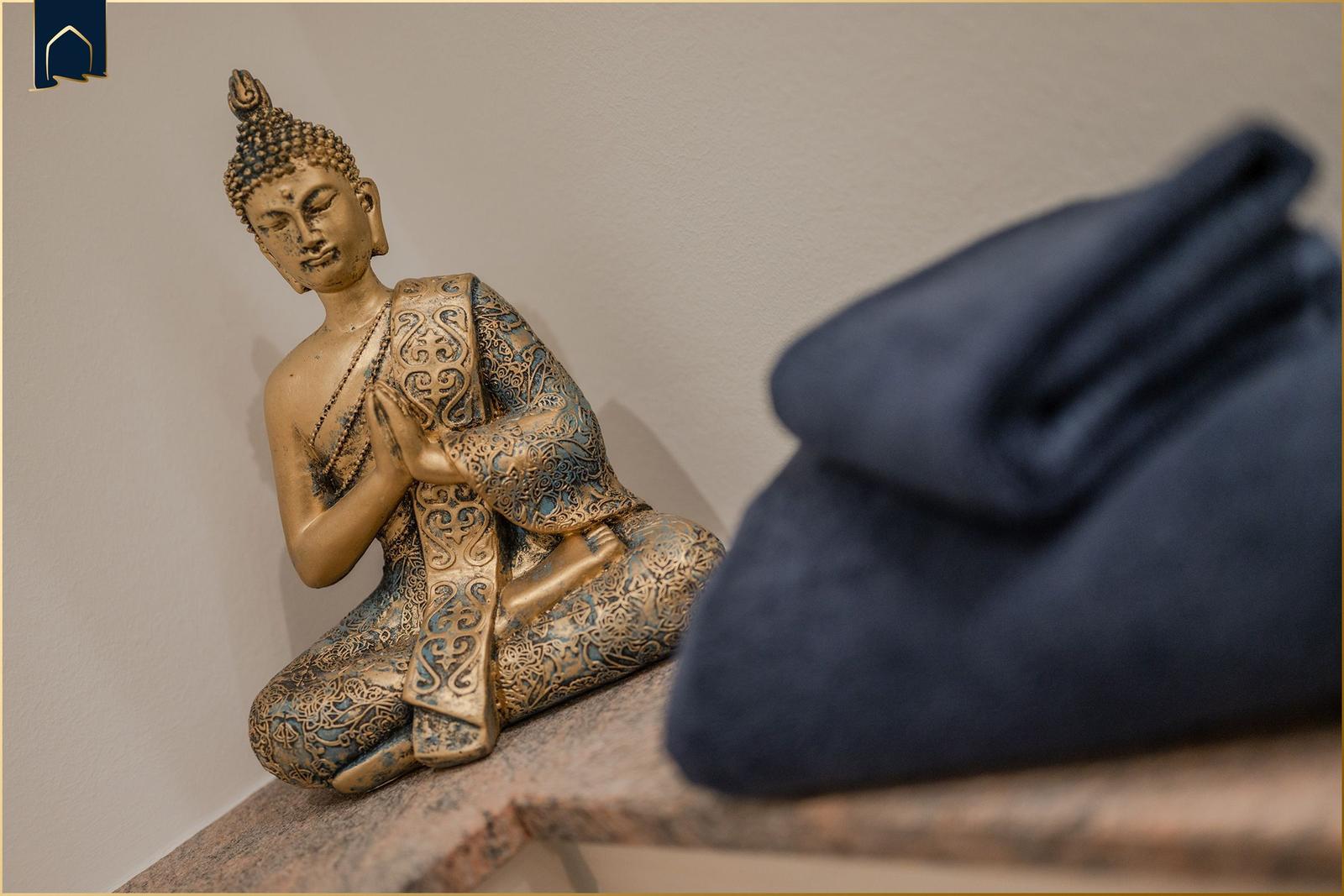 Buddha-Figur auf Steinbank neben blauem Kissen
