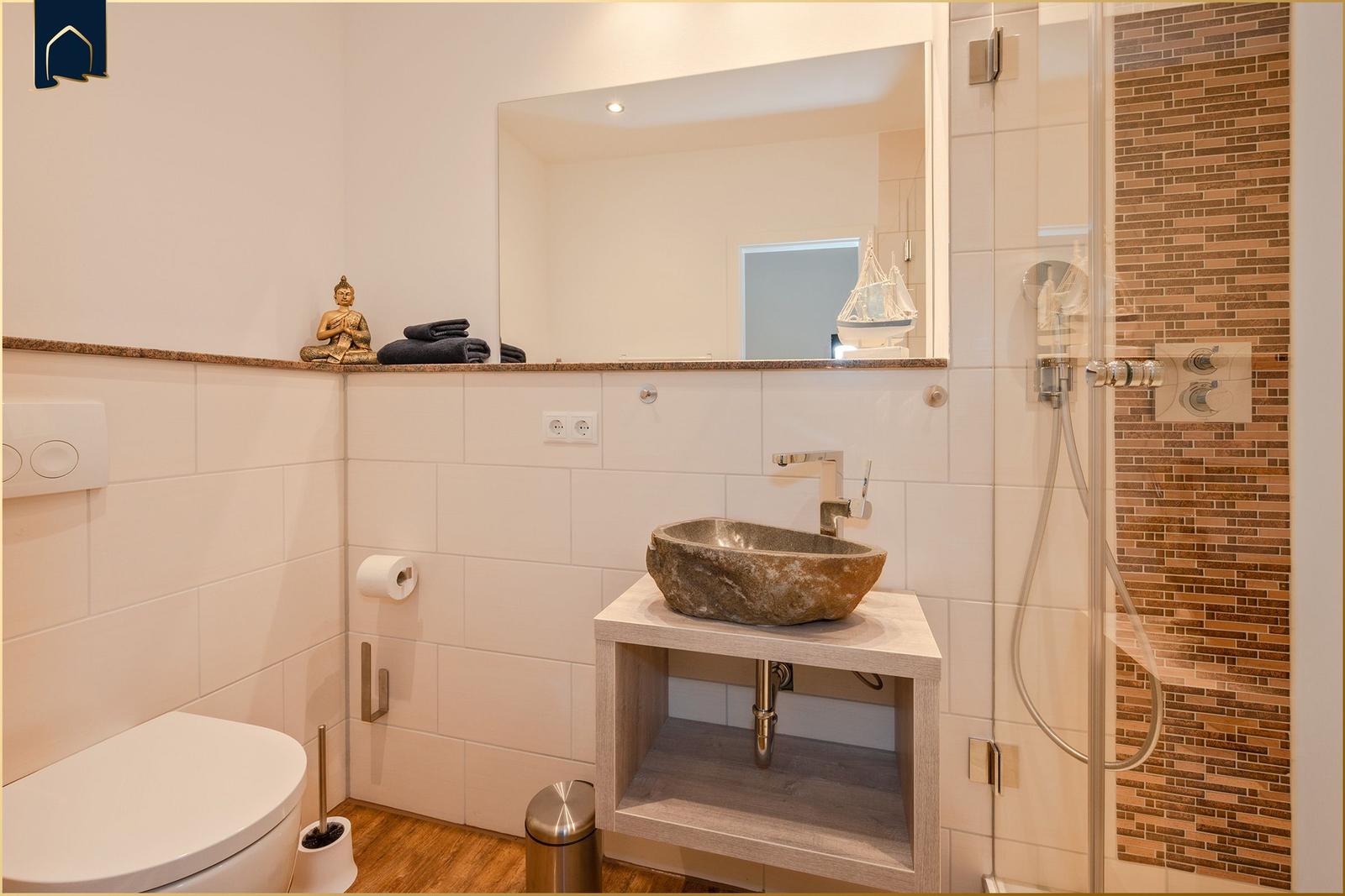 Badezimmer mit Steinwaschbecken, Dusche und Toilette. Spiegel und dekorative Gegenstände.