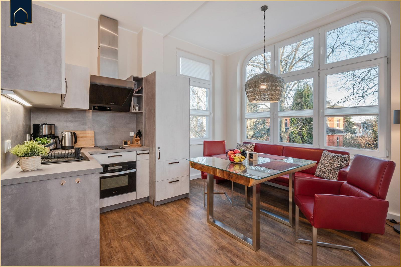 Küche und Essbereich mit rotem Sofa, Glas-Tisch und großen Fenstern.