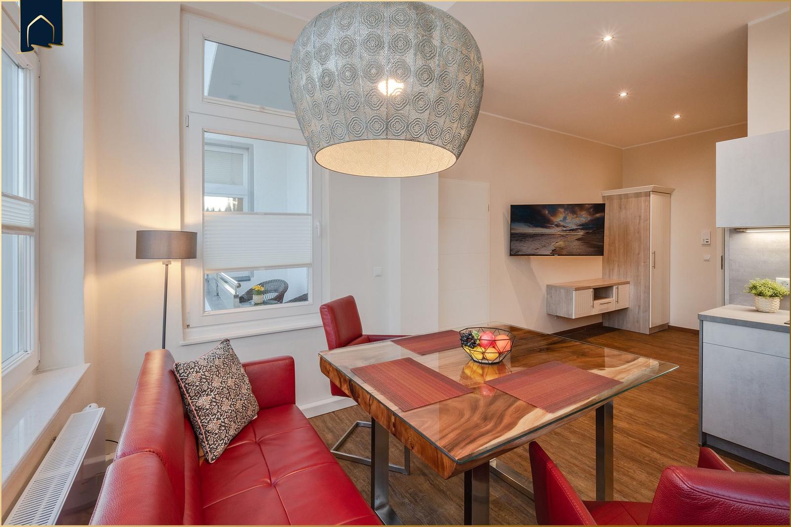 Ein Essbereich mit rotem Sofa, Glas-Tisch und einer großen Deckenleuchte.