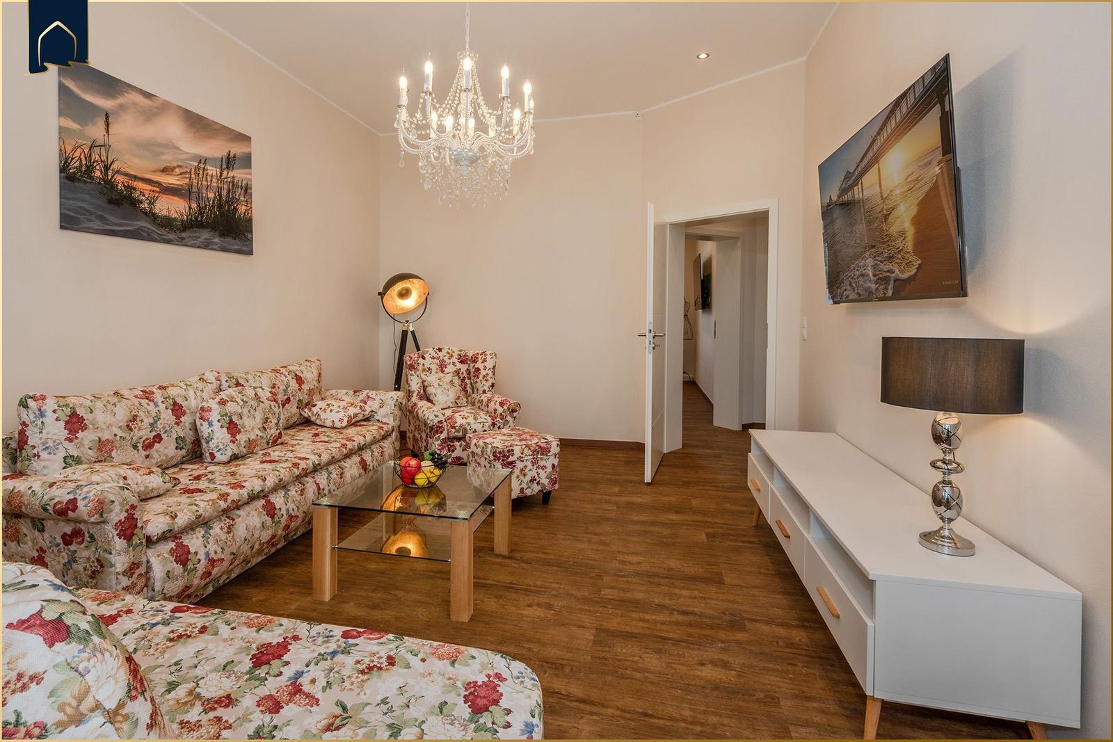 Wohnzimmer mit Sofa, Sessel und Fernseher an der Wand.