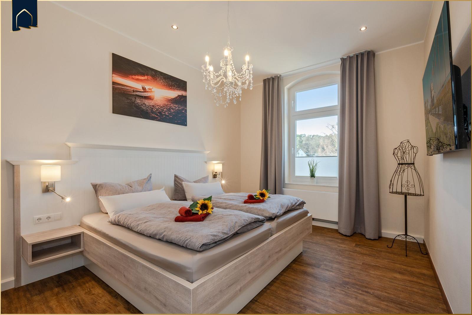 Schlafzimmer mit Doppelbett, Fenster, TV und Kronleuchter.
