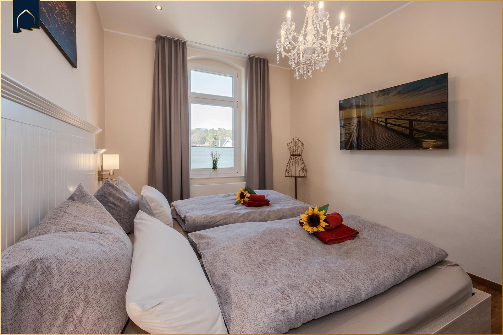 Doppelbett mit Sonnenblumen und roten Handtüchern, Fenster mit Blick, Kronleuchter und Wandbild.