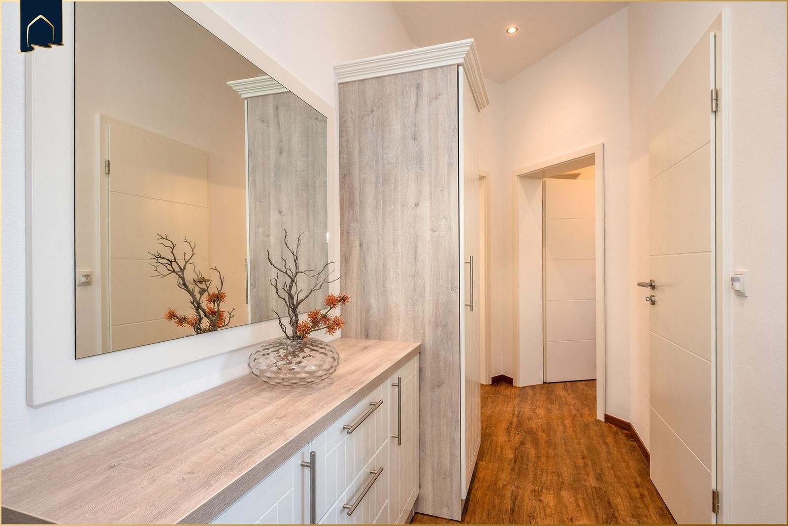 Flur mit Spiegel, Schrank und Holzboden. Dekorative Vase mit Zweigen auf Arbeitsplatte.