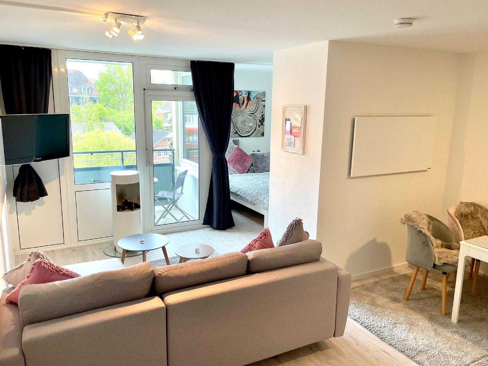 Wohnbereich mit Sofa, TV und Balkonzugang. Schlafzimmer im Hintergrund.