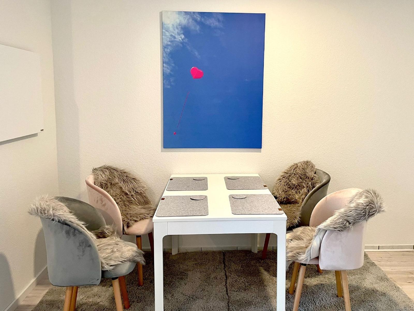 Esstisch mit vier Stühlen und Wandbild mit Herz.