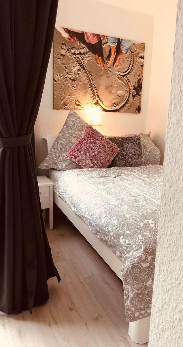 Schlafzimmer mit Bett, Kissen und Wandbild. Dunkle Vorhänge und Licht an der Wand.