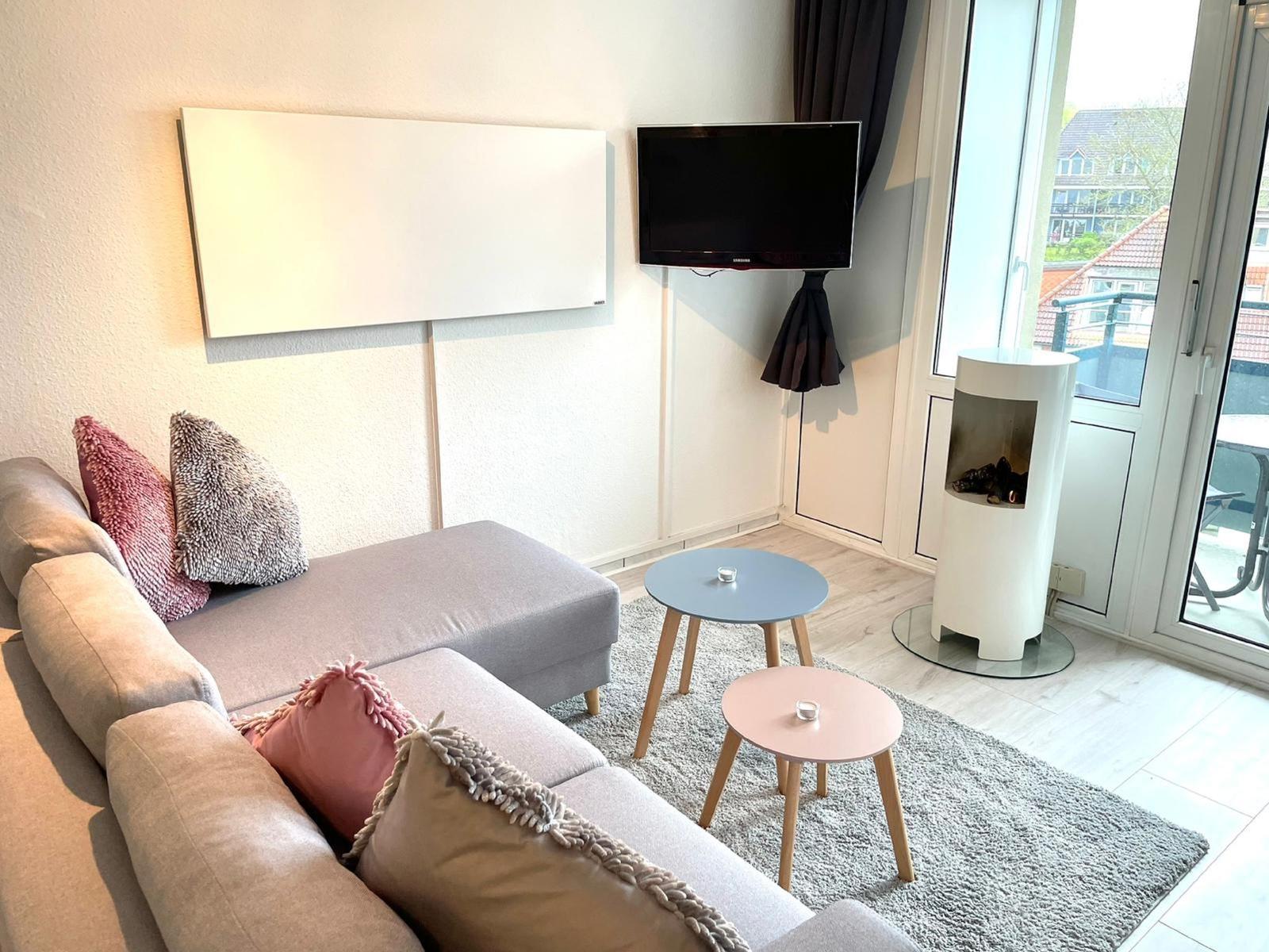 Ein Wohnzimmer mit Sofa, Fernseher und modernem Kaminofen. Durchgang zur Terrasse.