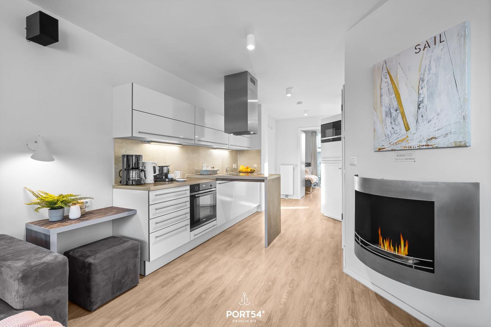 Küche mit Arbeitsfläche, Kühlschrank und Kaminofen mit brennendem Feuer.