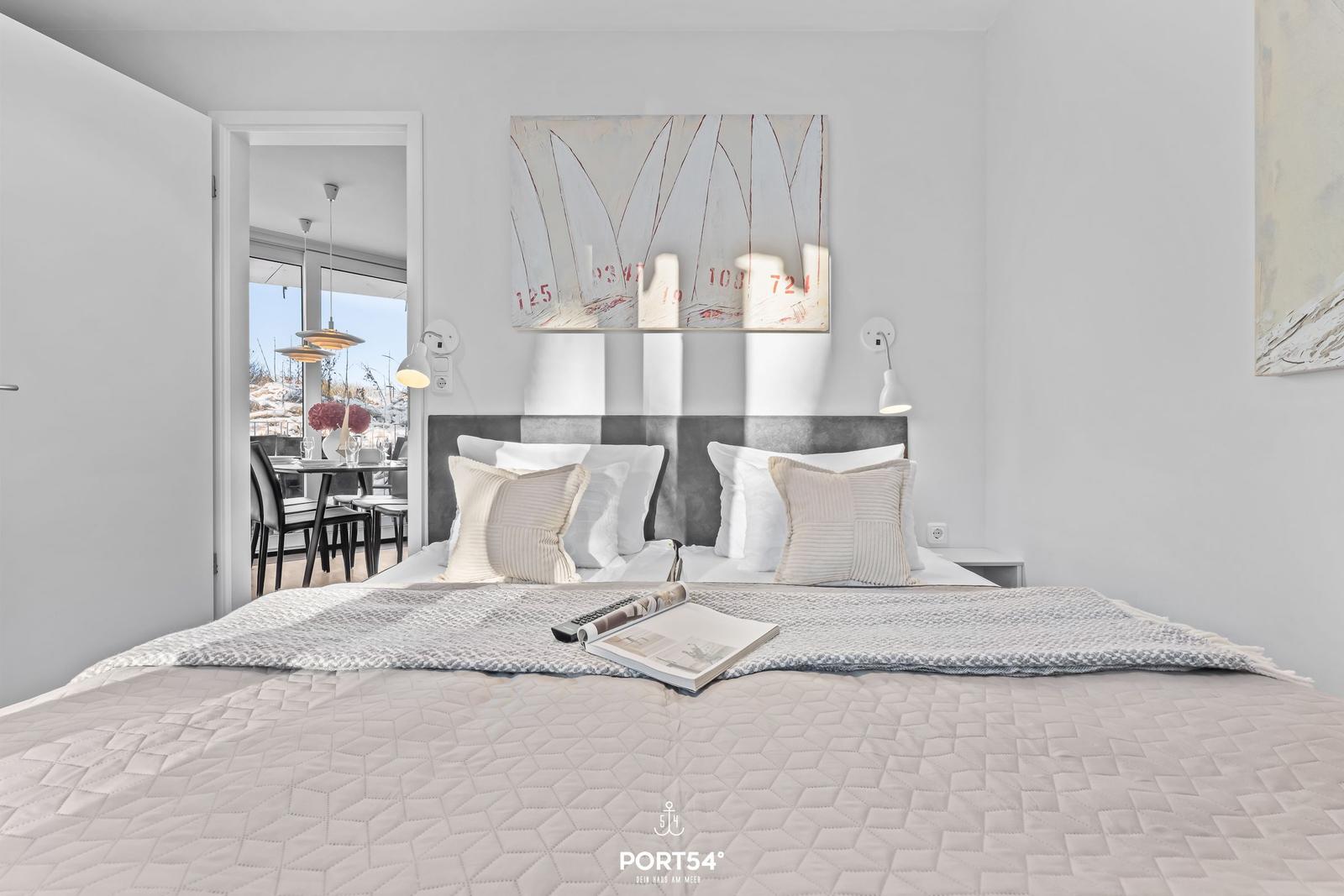 Schlafzimmer mit Bett, Wandbild und Blick in Essbereich.