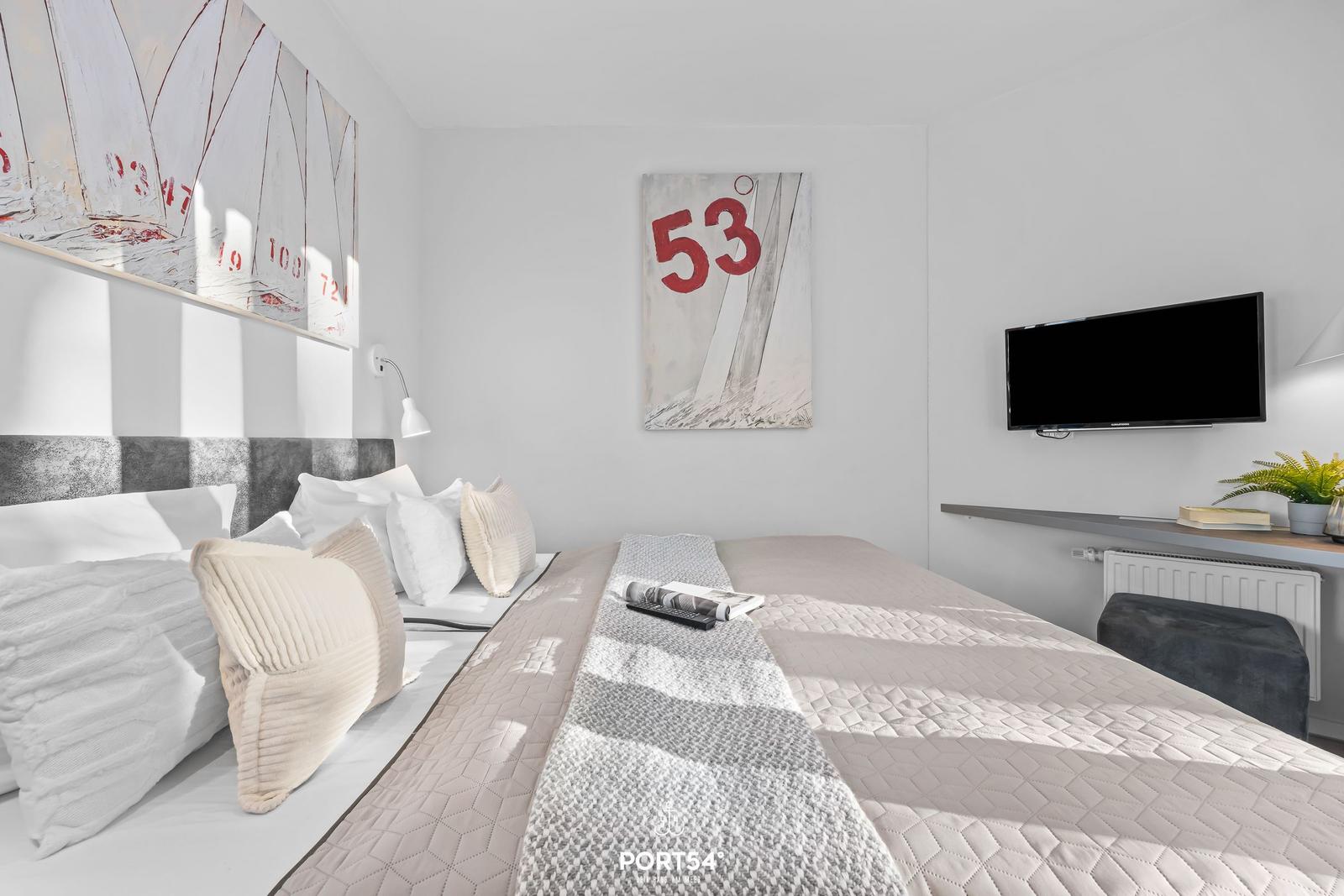 Schlafzimmer mit Bett, Wandbildern und Fernseher an der Wand.