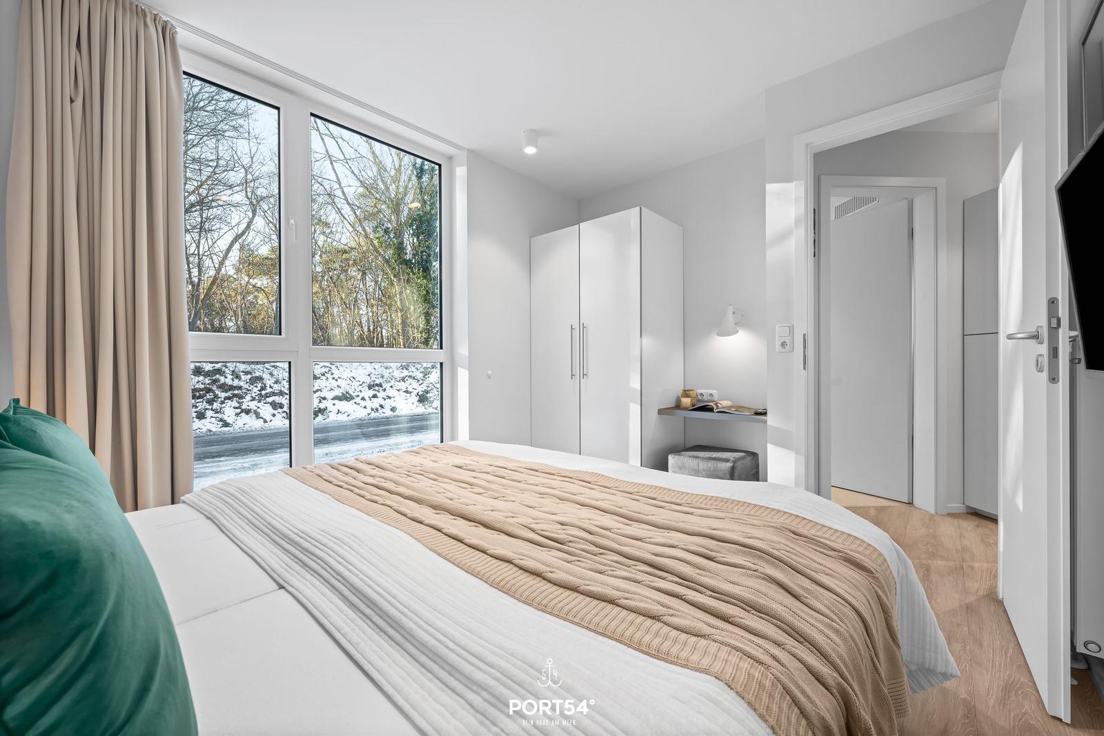 Schlafzimmer mit großem Fenster, Bett und Kleiderschrank.