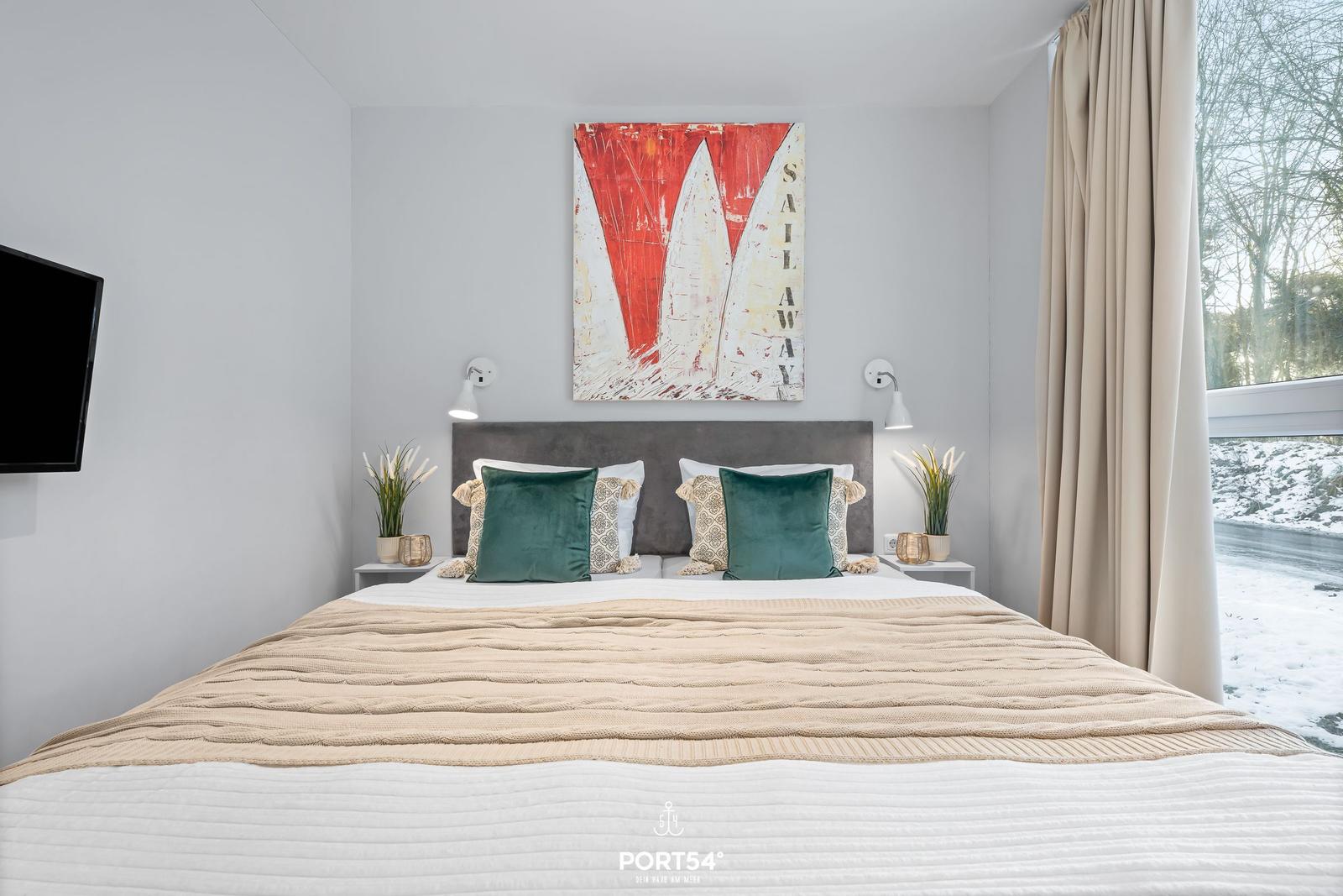 Schlafzimmer mit Bett, Wandbild und Fensterblick auf verschneite Landschaft.