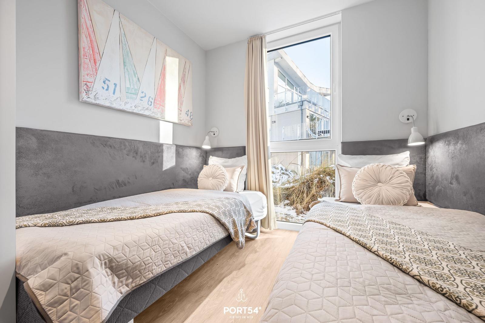 Zwei Betten mit grauem Kopfteil und gemusterten Bettdecken. An der Wand hängt ein Segelboot-Bild.