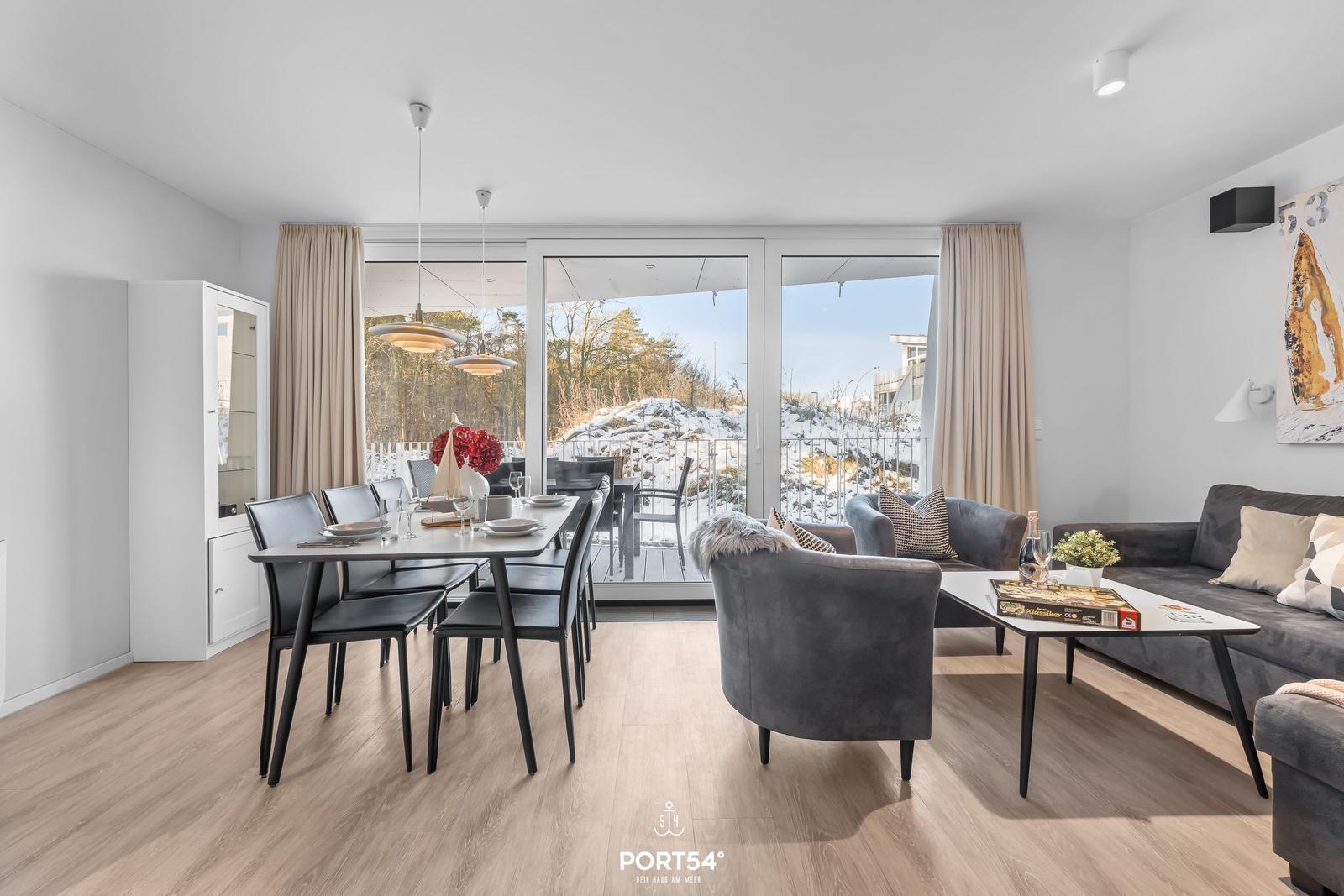 Wohn- und Essbereich mit Balkon, graue Sitzgelegenheiten und Holzboden.