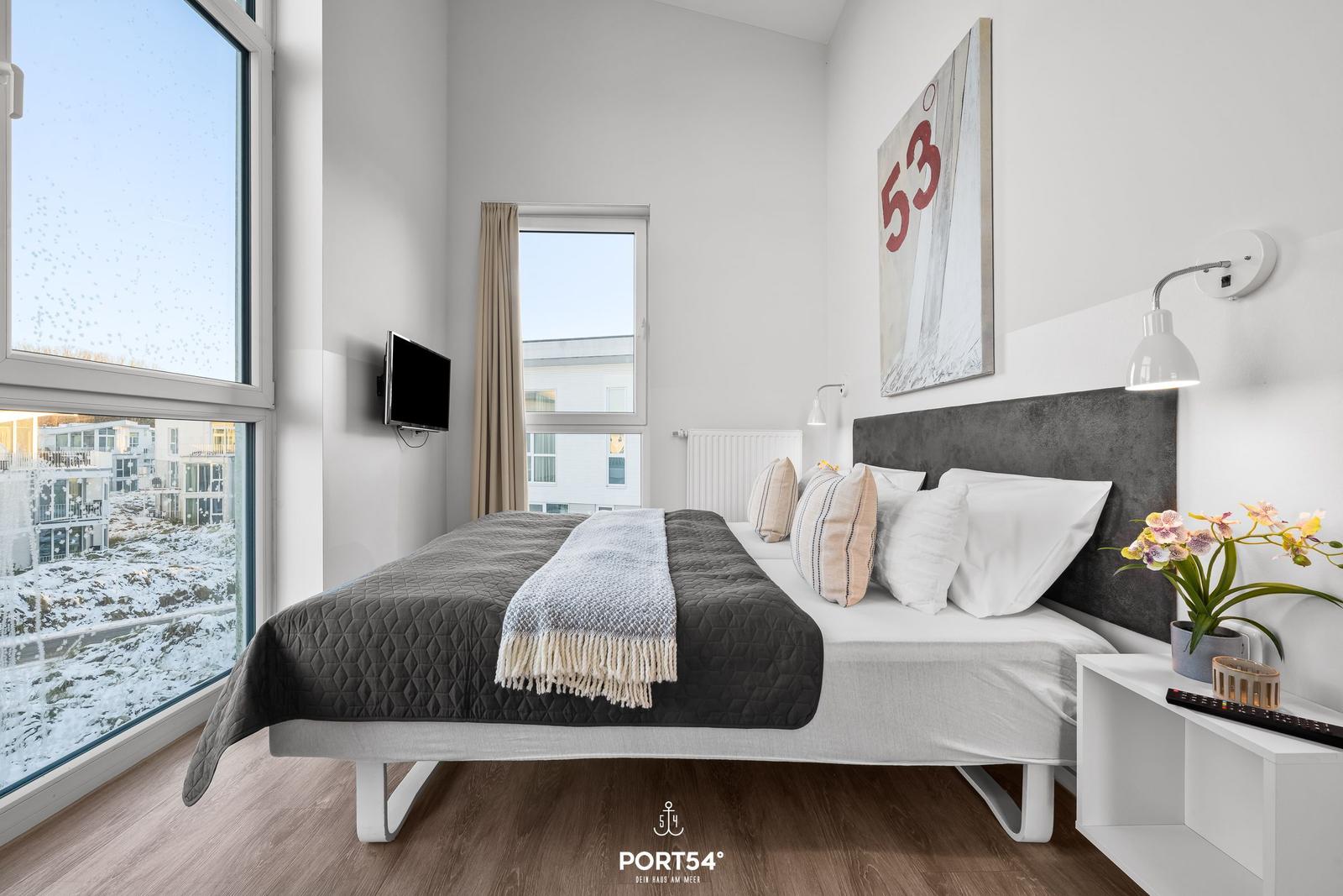 Schlafzimmer mit Bett, Fenstern und Wandbild. Blick auf verschneite Landschaft.