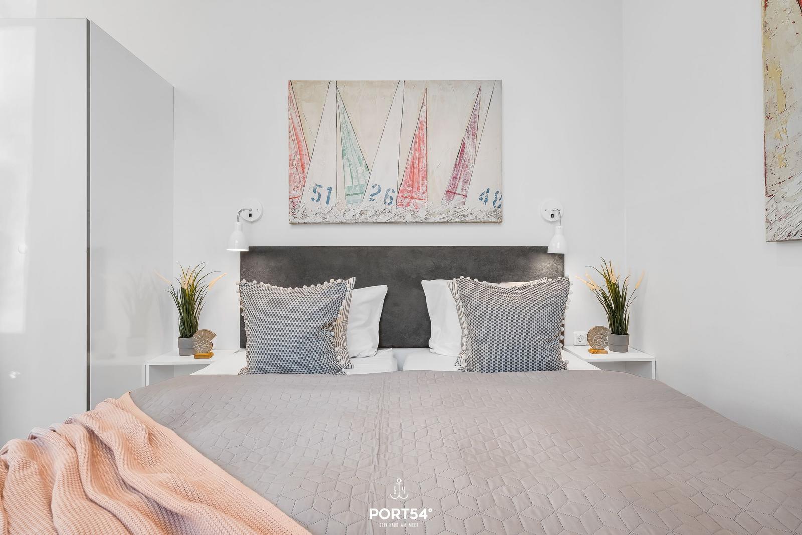 Schlafzimmer mit Bett, Wandbild und Nachttischen.