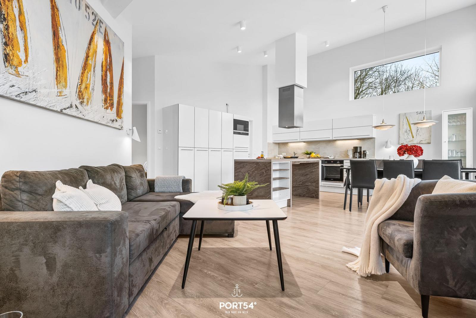 Wohn- und Küchenbereich mit grauem Sofa, Esstisch und moderner Küche.