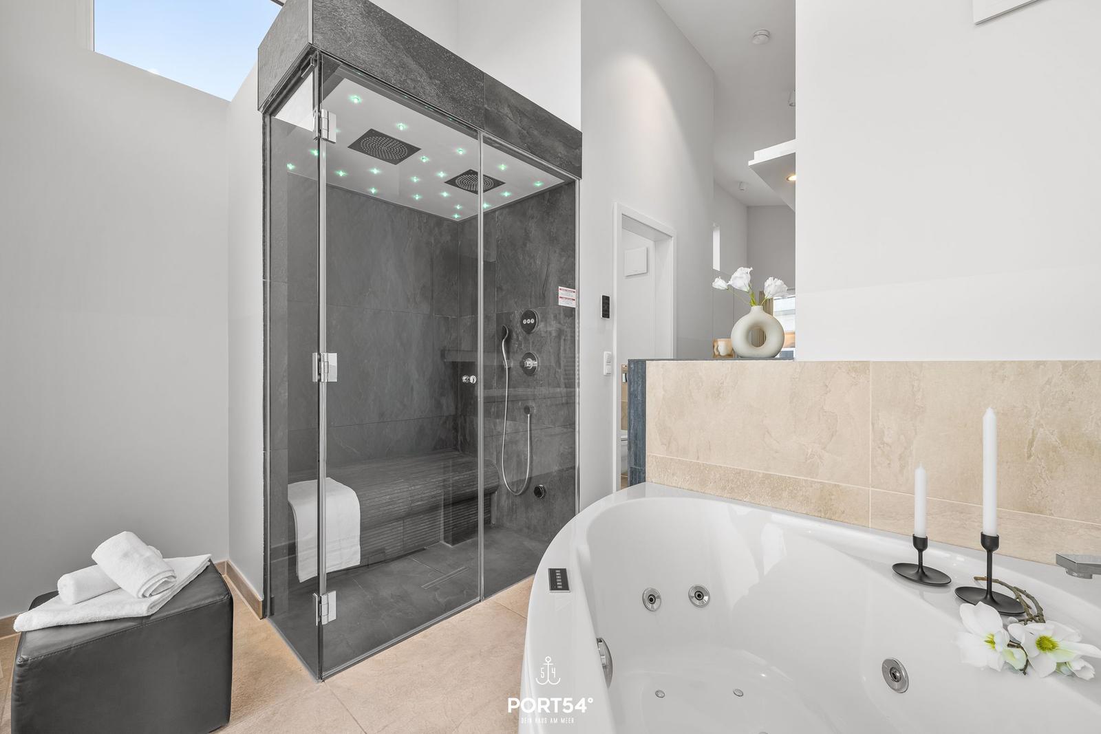 Dusche mit LED-Beleuchtung und Whirlpool-Badewanne mit Kerzen und Blumen.