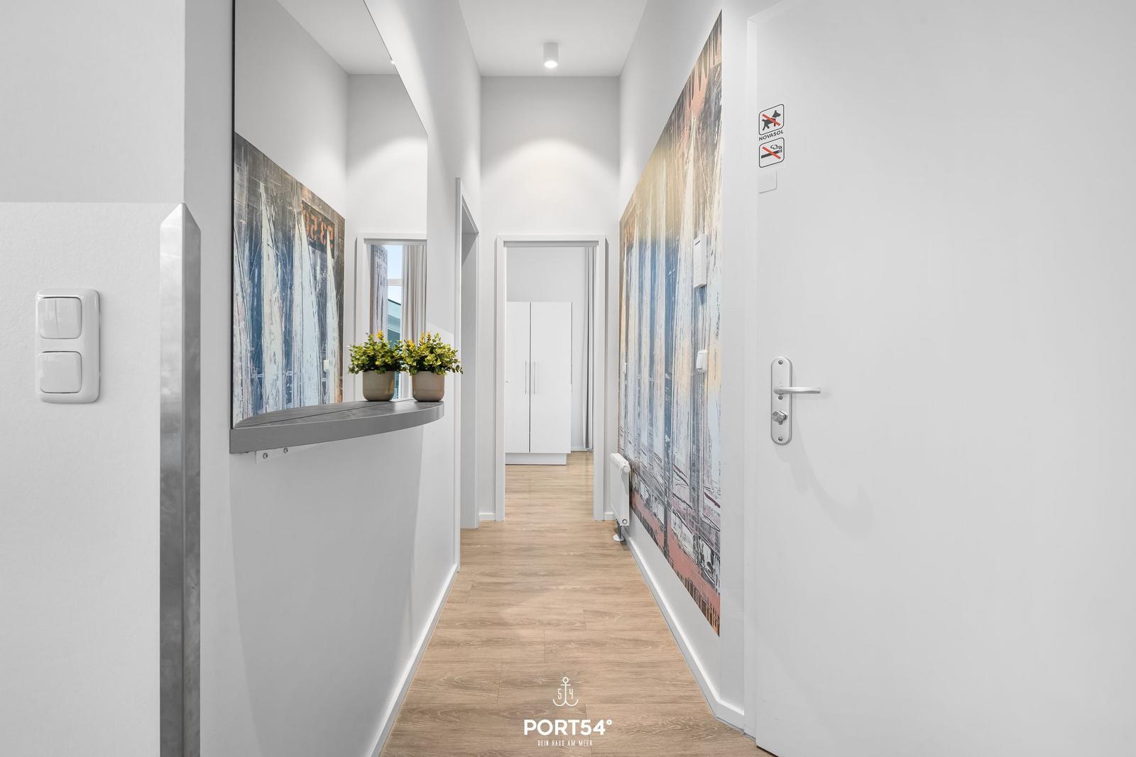 Flur mit Holzboden, Wandbildern und Pflanzen. Tür und Schalter sind sichtbar.