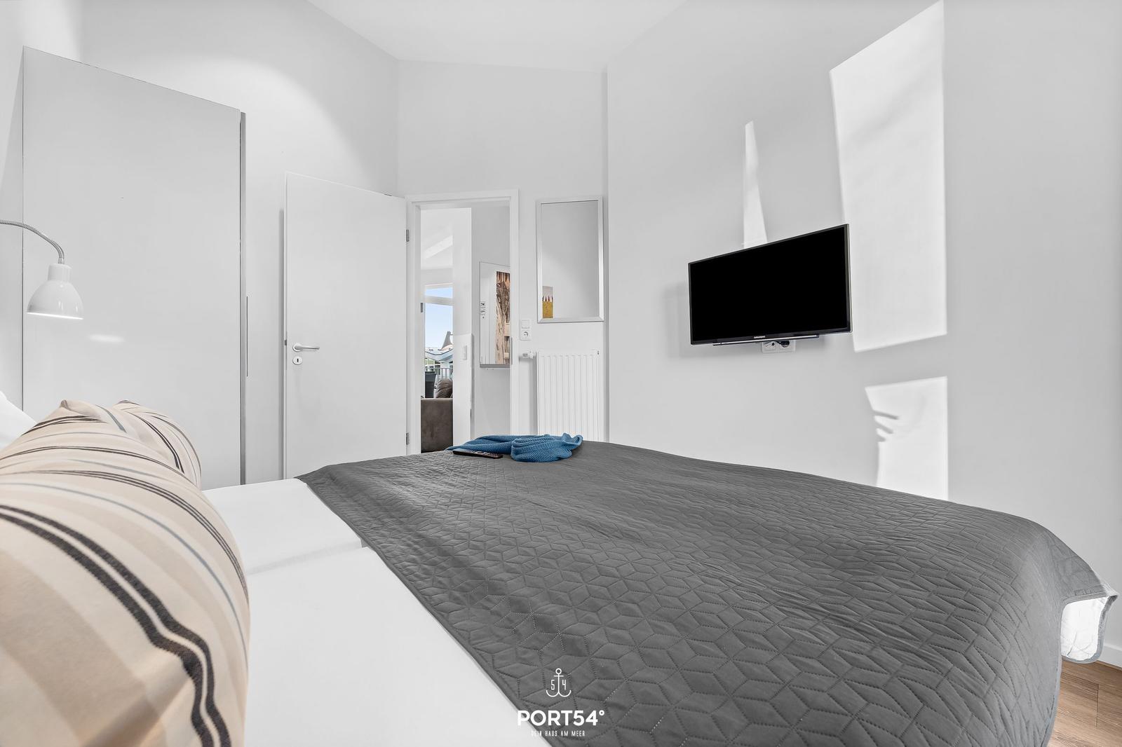 Schlafzimmer mit Bett, Wand-TV und Tür zum Flur.