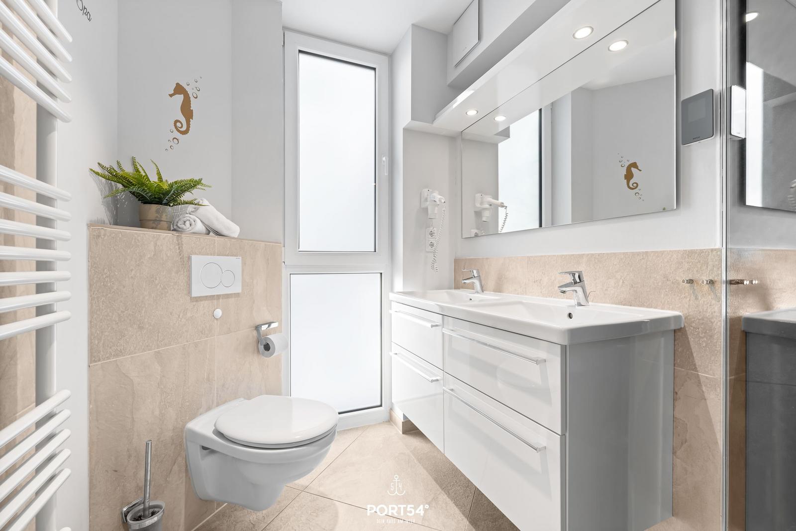 Badezimmer mit Toilette, Waschbecken und Dusche. Wanddekoration mit Seepferdchen.