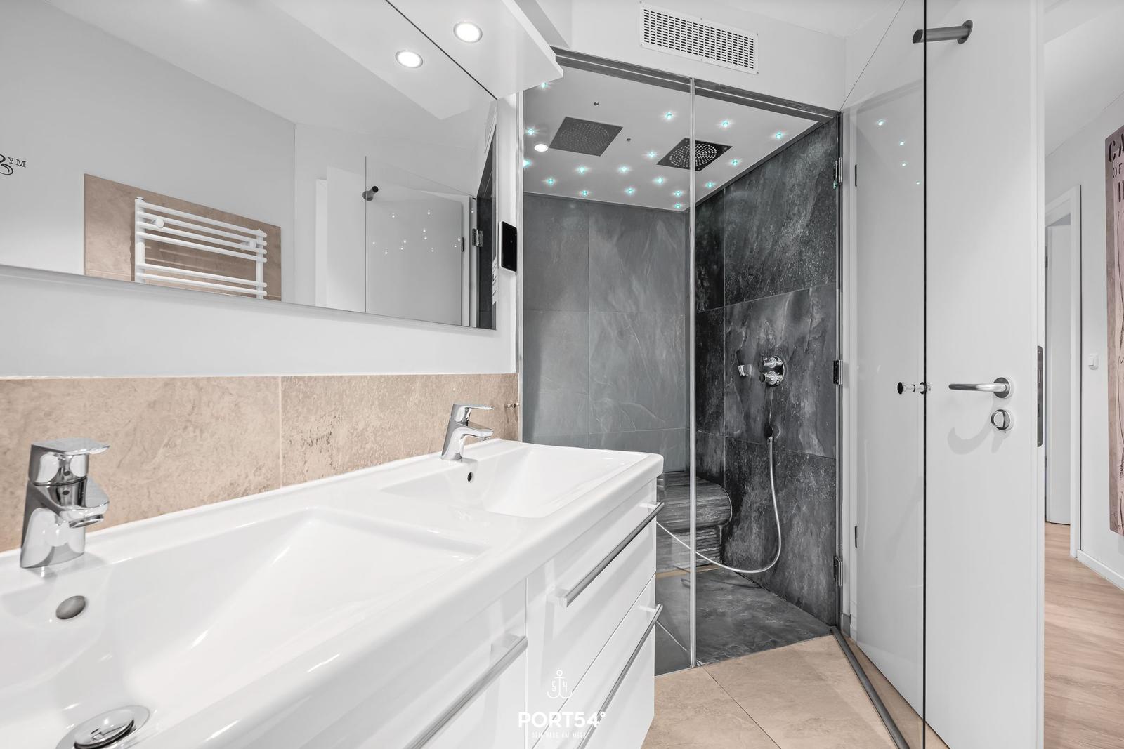 Badezimmer mit Dusche, Waschbecken und Spiegel.