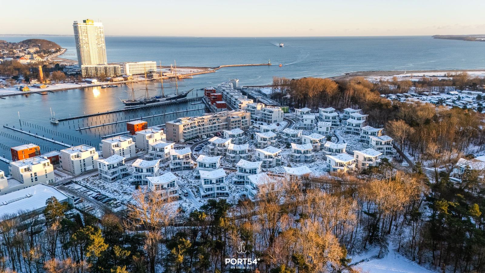 Schneelandschaft mit modernen Häusern am Hafen und Blick aufs Meer.