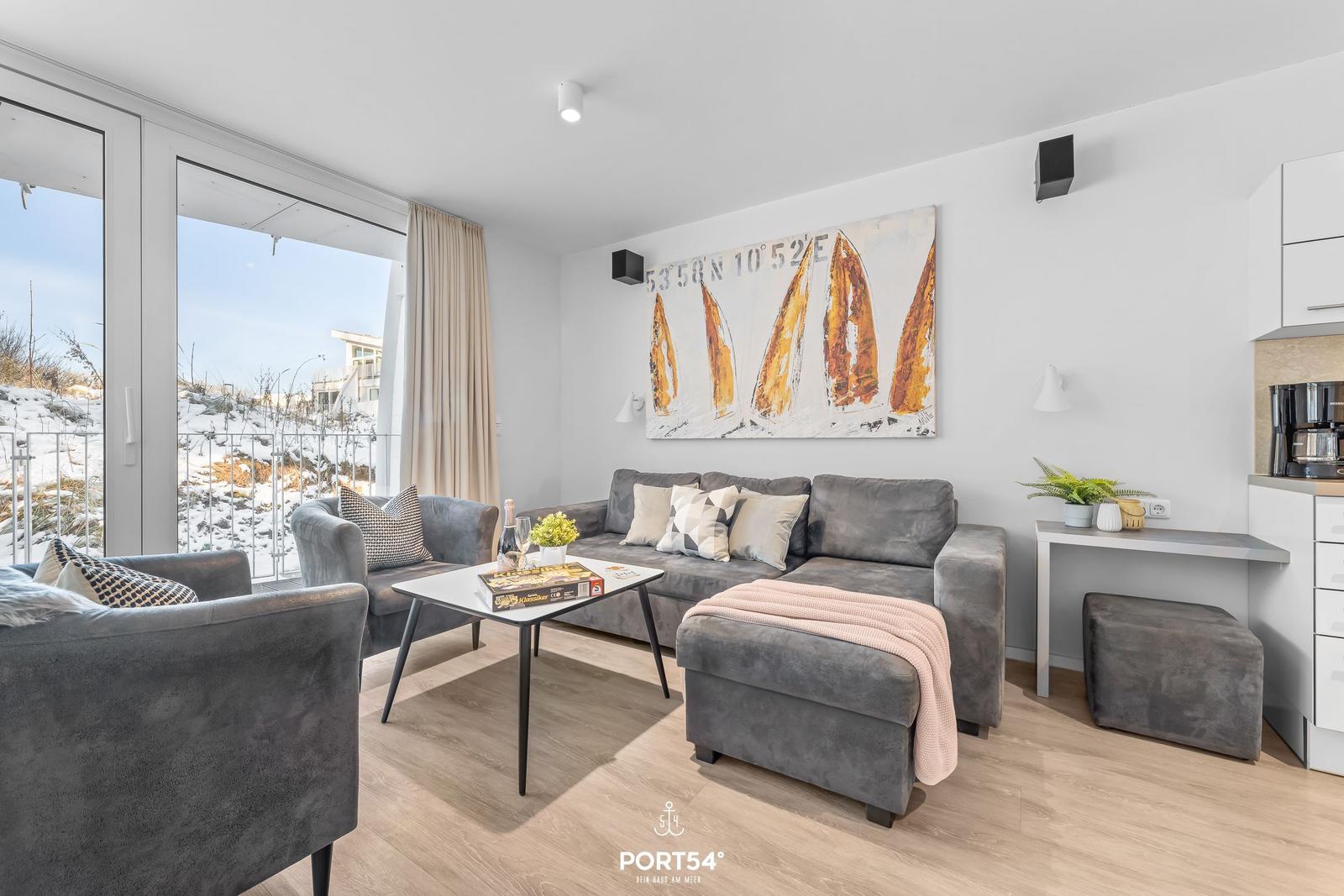 Wohnzimmer mit Sofa, Sessel und Blick auf verschneite Landschaft.