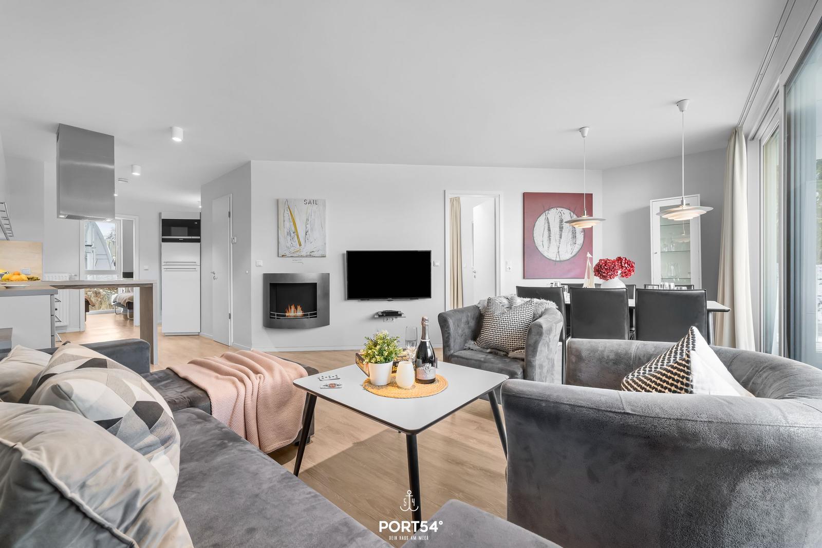 Wohn- und Essbereich mit Kamin, Sofa und Esstisch. Küche im Hintergrund.