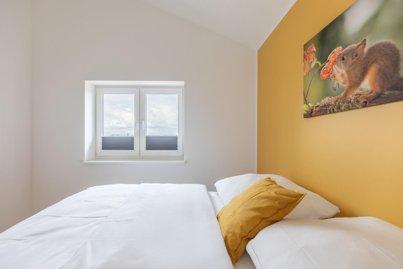 Schlafzimmer mit Bett, Fenster und Wandbild eines Eichhörnchens.