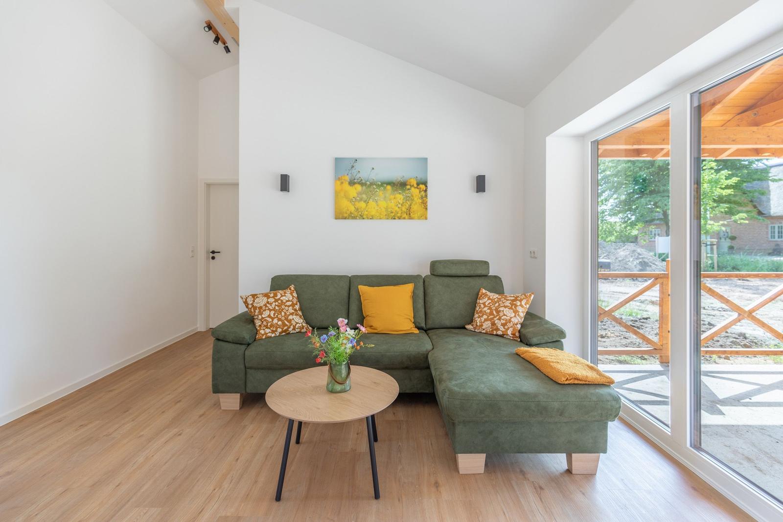 Ein Wohnzimmer mit grünem Sofa, Holzboden und großem Fenster zur Terrasse.