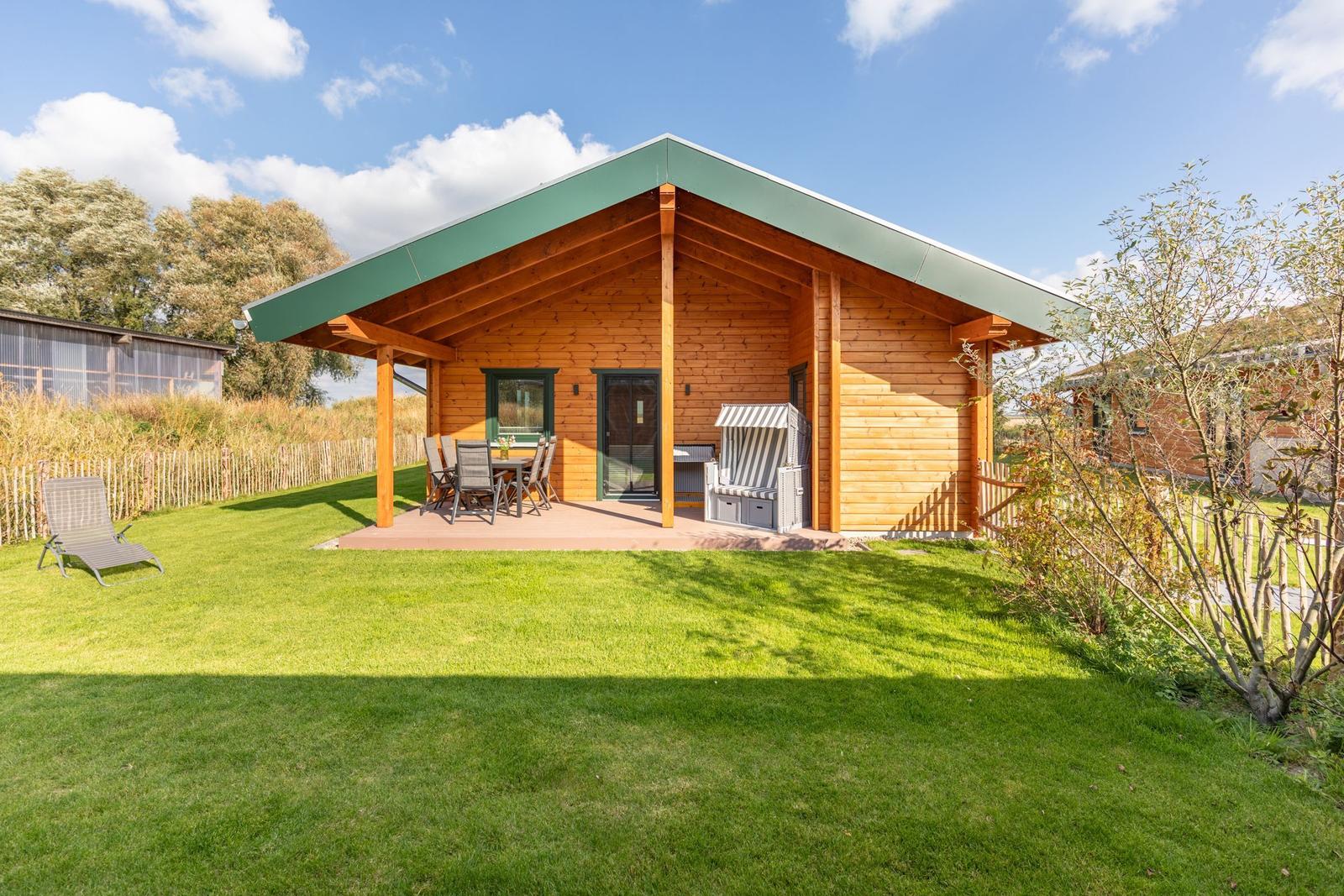 Holzhaus mit Terrasse, Garten und Liege. Grün-dach und Möbel sichtbar.