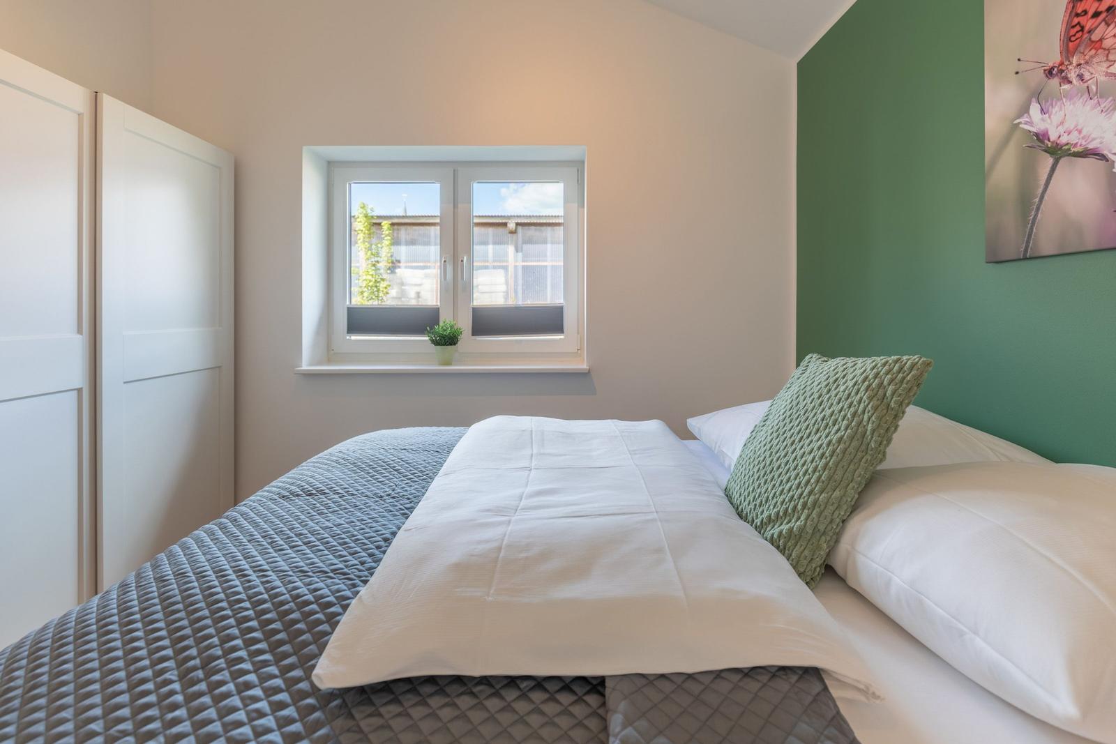 Schlafzimmer mit Bett, Fenster und grüner Wand. Wandbild mit Schmetterling.