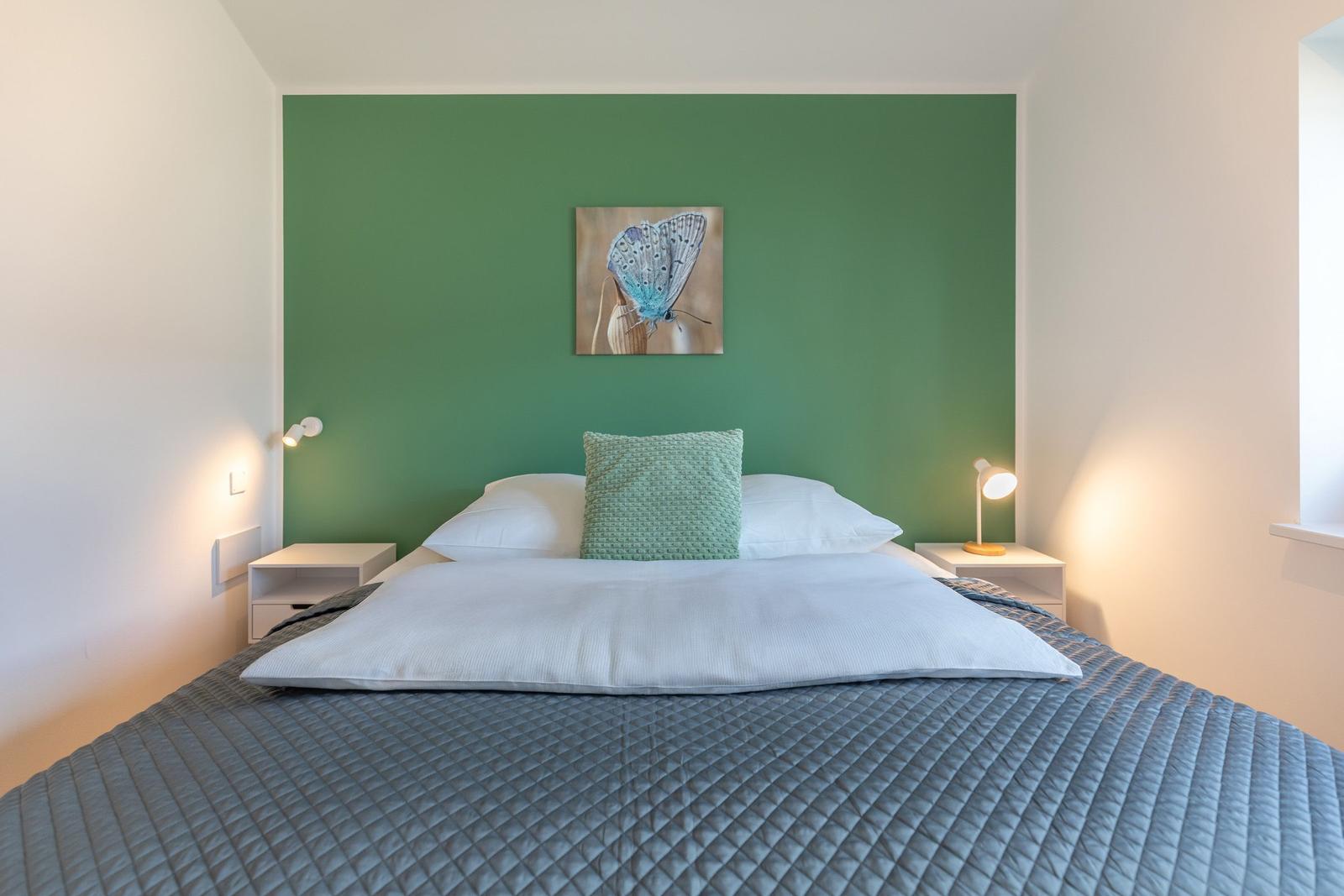 Schlafzimmer mit grünem Wandabschnitt, Bett mit Kissen und Nachttischen mit Lampen.