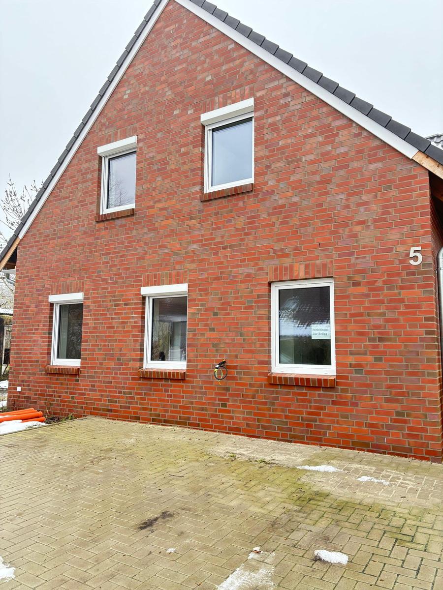 Holiday home with red brick facade and white windows. House number 5. Front yard with paving stones.