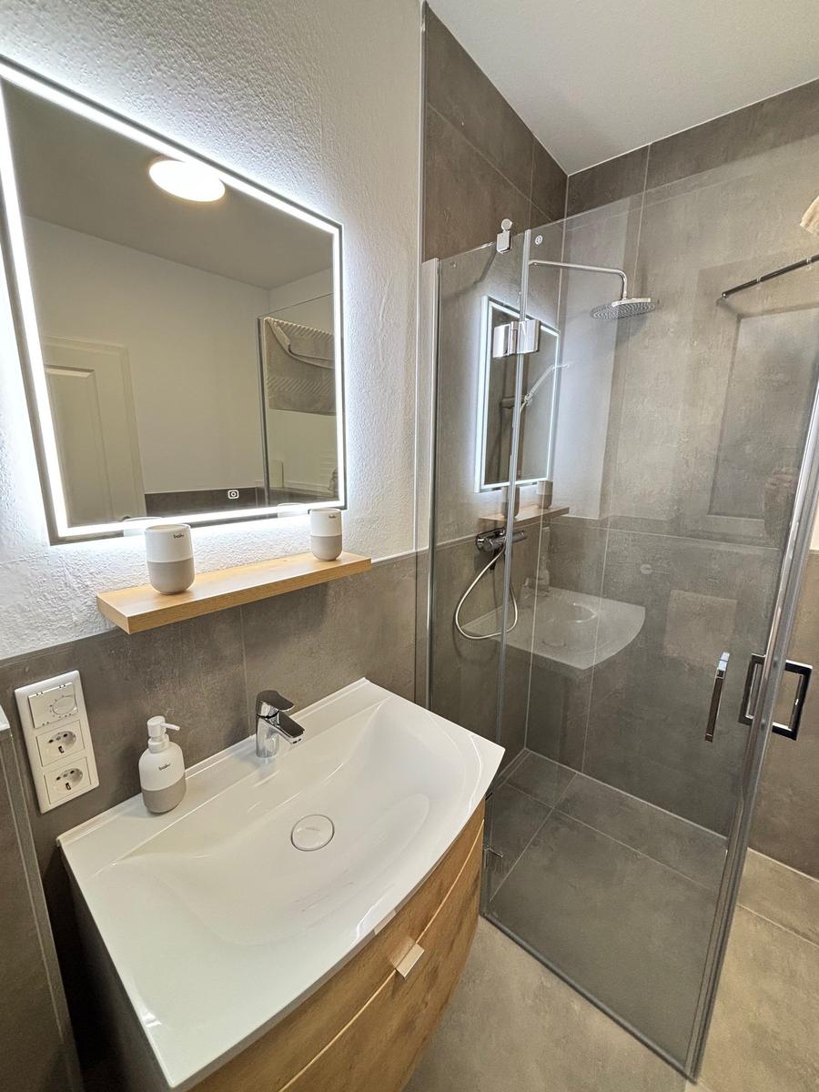 Bathroom with shower, sink, and lit mirror.