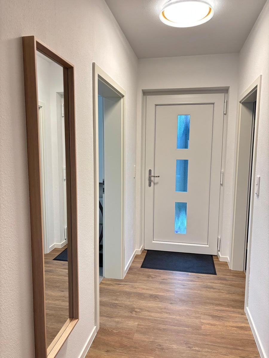 Hallway with wooden floor, mirror, and entrance door with blue glass panels.
