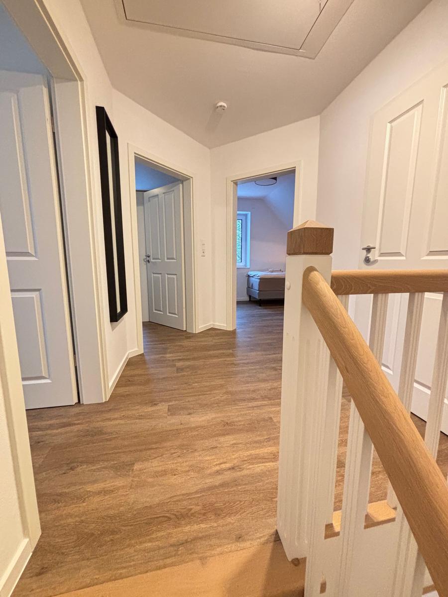 Hallway with wooden floor and staircase to upper floor. Doorways to bedrooms and bathroom.