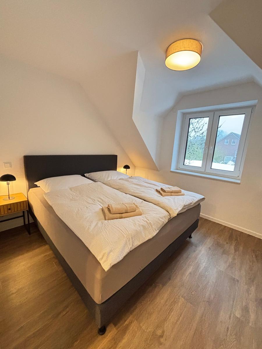Bedroom with double bed, wooden floor, and window. Ceiling light and bedside table visible.