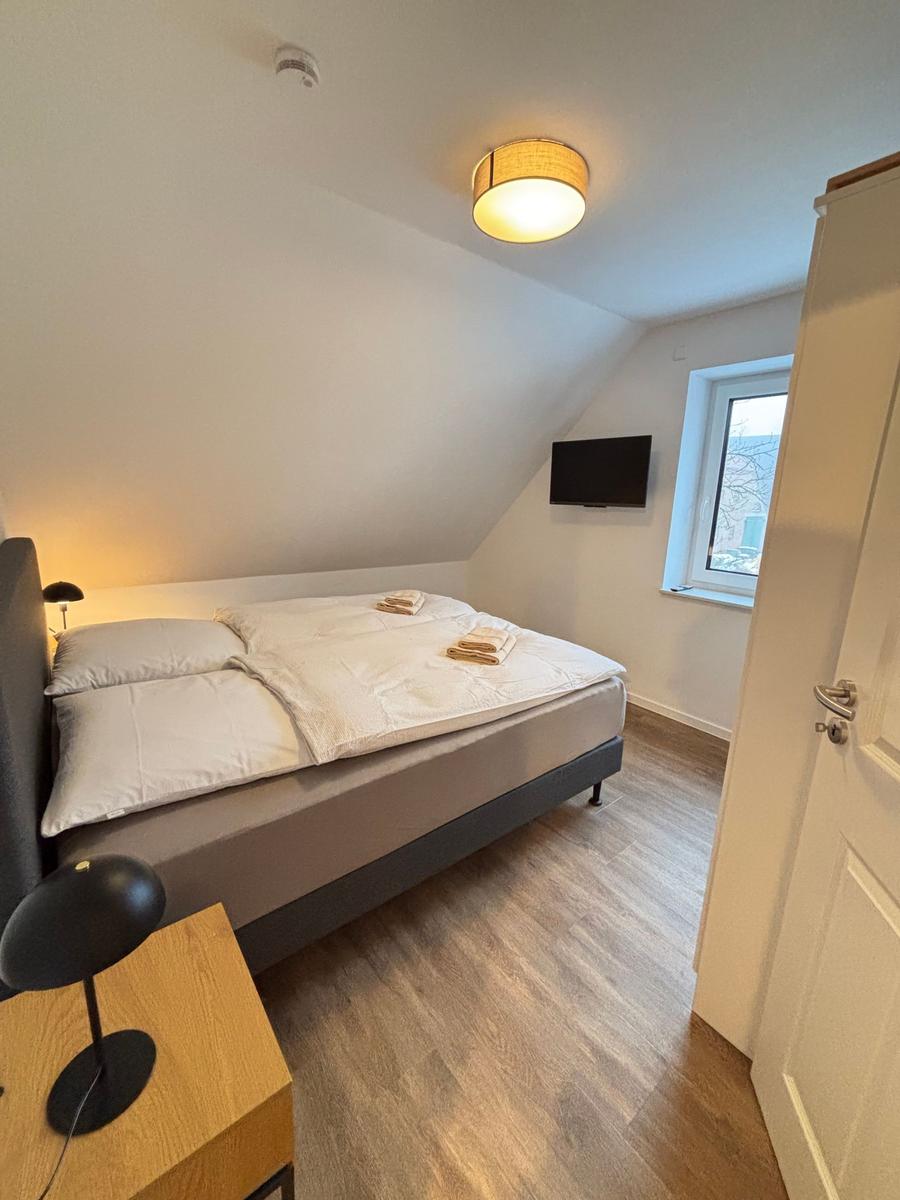 Bedroom with double bed, TV, and window. Wooden floor and ceiling light.